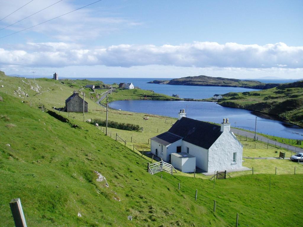 a small white house on a hill with a body of water at Harris White Cottage in Rodel