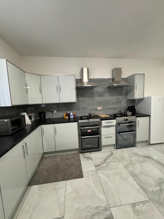a kitchen with white cabinets and black appliances at Chief Vic Guest house in Oldham