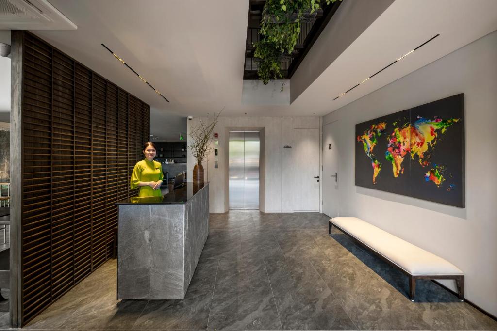 A compact reception desk stands beside a hallway with a bench, artwork, and elevator doors.