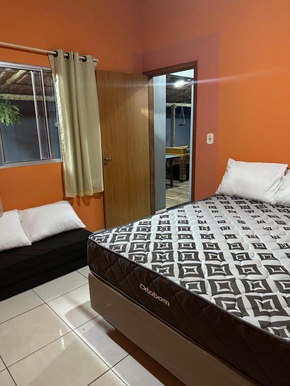 a bed in a room with an orange wall at Sítio Recanto da Mata 1 suíte, 2 quartos, área de piscina, churrasco, área de jogos, campo de vôlei, lago para pesca, moenda de cana e rede para descanso in Marataizes