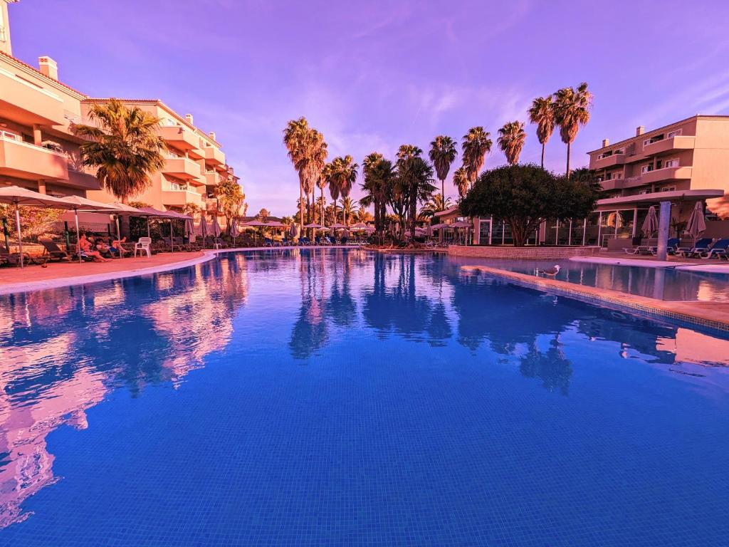 a large swimming pool with palm trees and buildings at VilaFplaza by JohnVillas in Portimão