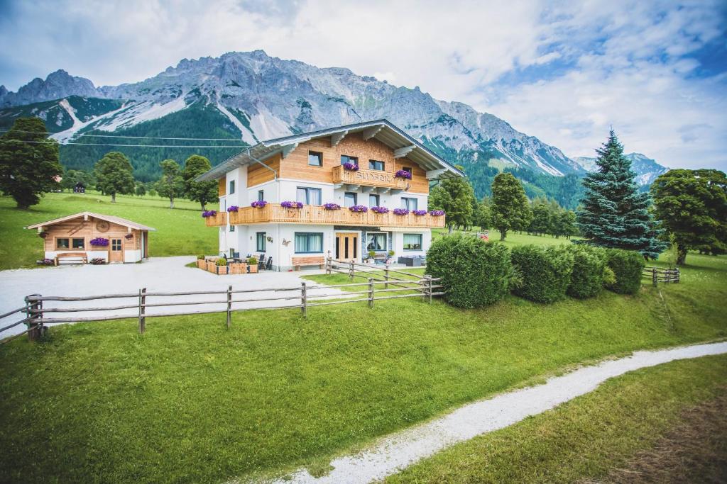 a house in a field with mountains in the background at Landhaus Sunseitn in Ramsau am Dachstein