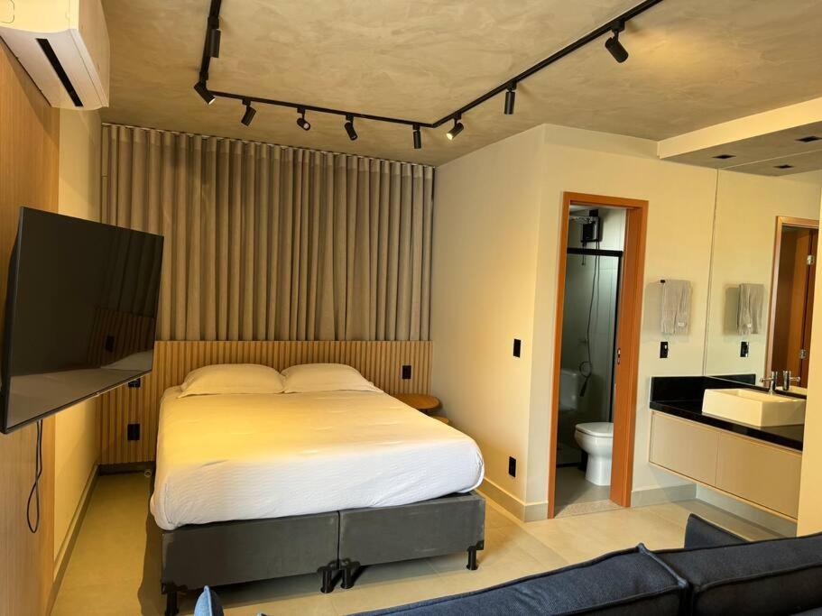 a bedroom with a bed and a tv and a bathroom at Apto Novo próx Center Shopping in Uberlândia