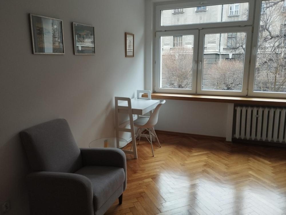 een woonkamer met een stoel, een tafel en 2 ramen bij Apartament Parkowy in Bielsko-Biala