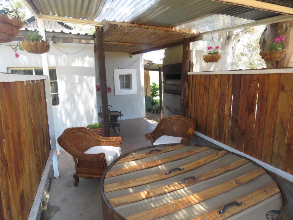 - une terrasse couverte avec un lit en bois et 2 chaises dans l'établissement Swartberg Backpackers, à Matjiesrivier