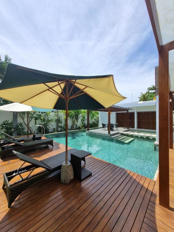 a swimming pool with an umbrella and chairs and a table at Villa Capella in Canggu