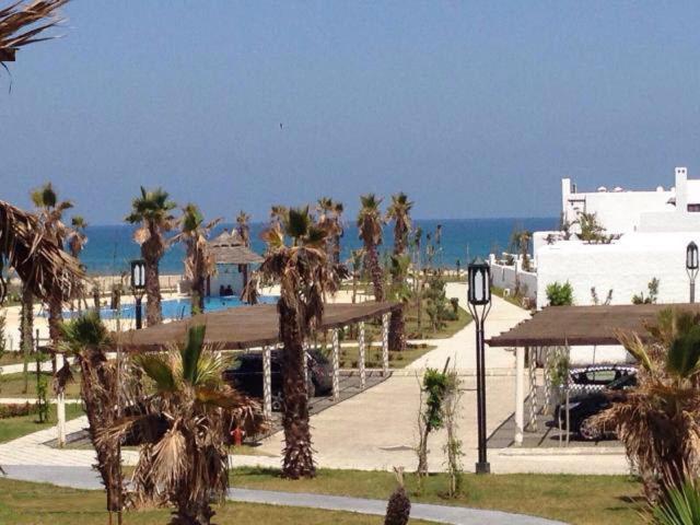 a street with palm trees and a building and the ocean at Apartment Cabo Negro Royal Golf and Resort in Cabo Negro