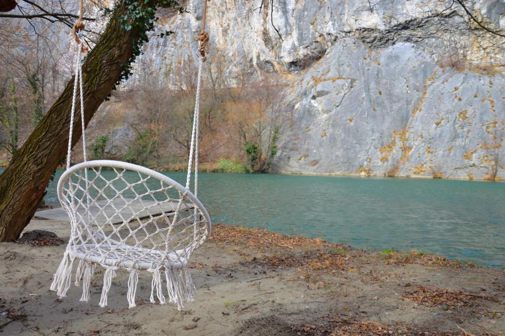 a white chair hanging from a tree next to a river at Vikendica Banjska Diva in Ovčar Banja