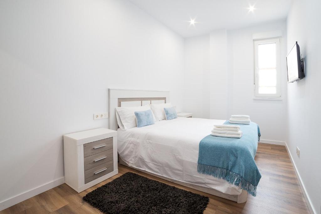 Dormitorio blanco con cama blanca y manta azul en Salamanca Confort Estudios A y B, en Salamanca