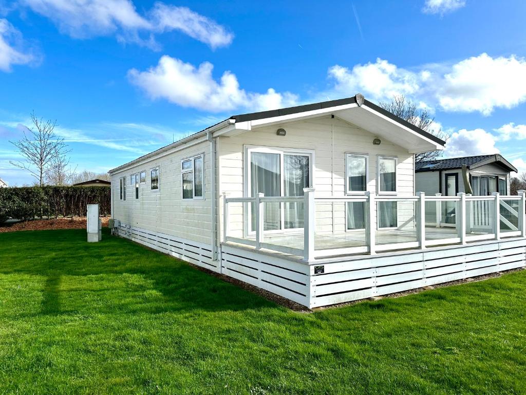 a small white house on a grass field at Bluebell Lodge, Dog Friendly in South Cerney