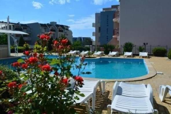 a swimming pool with white chairs and red flowers at Sem.hotel -Afrikana in Sveti Vlas