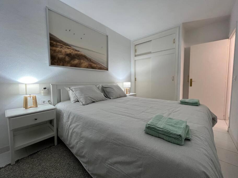 a bedroom with a white bed with a nightstand and a picture at Precioso Apartamento en Es Grau in Es Grau