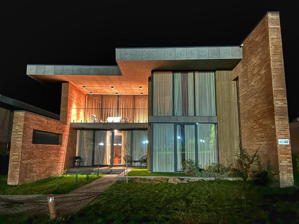 a large brick house with glass windows at night at Villa #40 in Kachretʼi