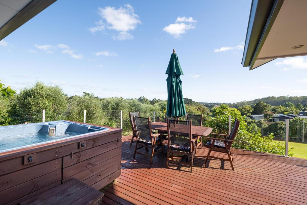 a deck with a table and an umbrella and a hot tub at RidgeRaj - Kerikeri Holiday Home in Kerikeri