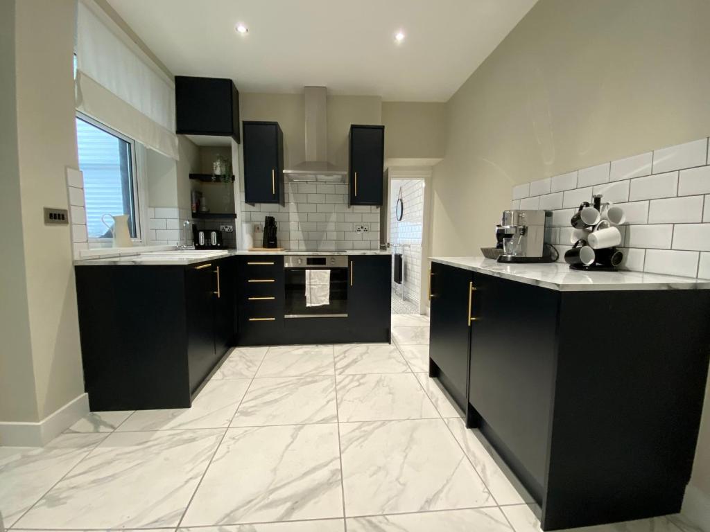 a large kitchen with black cabinets and white tile floors at Newly renovated, hi-spec three bed, forest view home in Cwmcarn