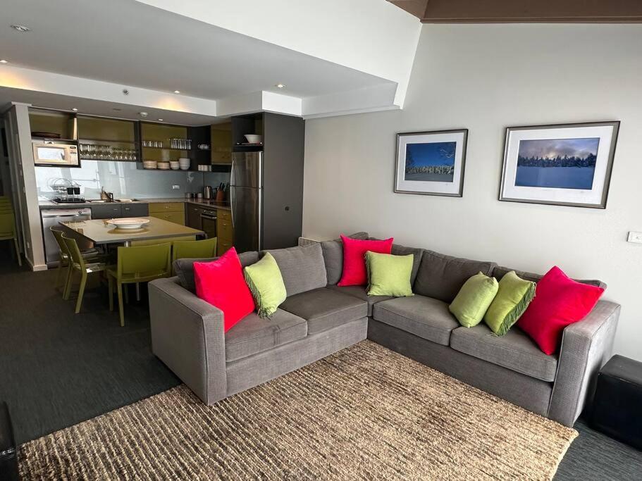 una sala de estar con un sofá gris con almohadas rojas y verdes en White Crystal 210 Ski In, Ski Out, en Monte Hotham