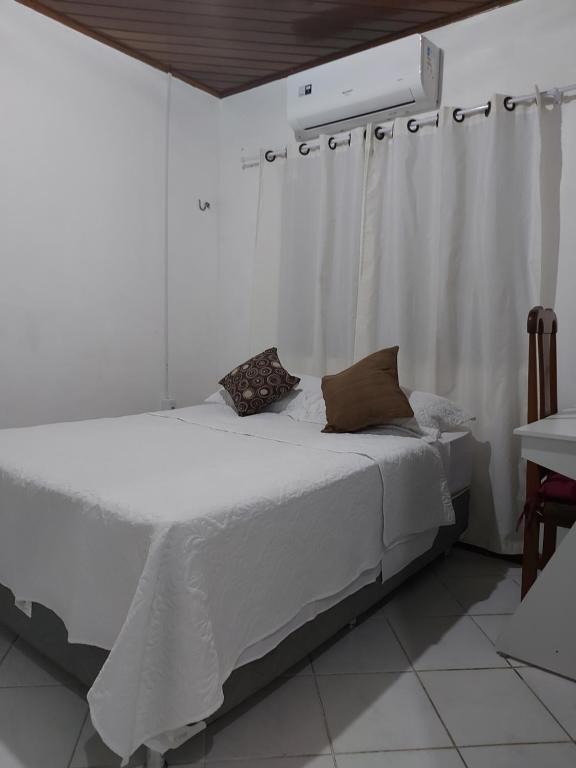 uma cama branca com duas almofadas num quarto em Suíte com ar condicionado próximo ao Estádio Mangueirão em Belém