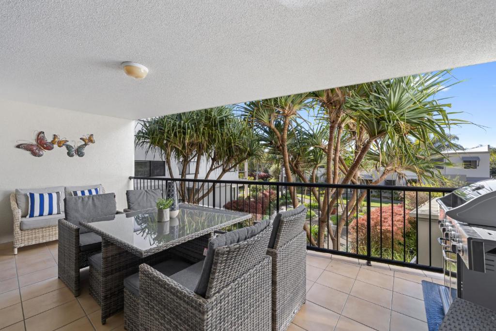 a balcony with a table and chairs and palm trees at Beachside 3-Bed with Pool, BBQ, Gym & Tennis Court in Marcoola