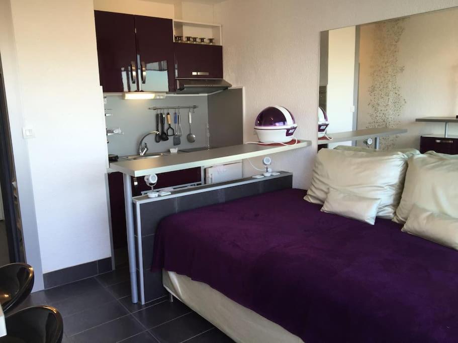 Cet appartement comprend une chambre avec un lit violet et une cuisine. dans l'établissement Studio 18, Héliopolis L au village naturiste, au Cap d'Agde