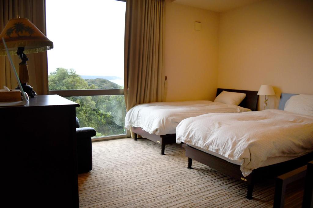 two beds in a hotel room with a large window at Ocean View Luxury Beach House - Enjoy Spring Cherry Blossoms, Beaches and BBQ at a Luxury Home in Shimoda