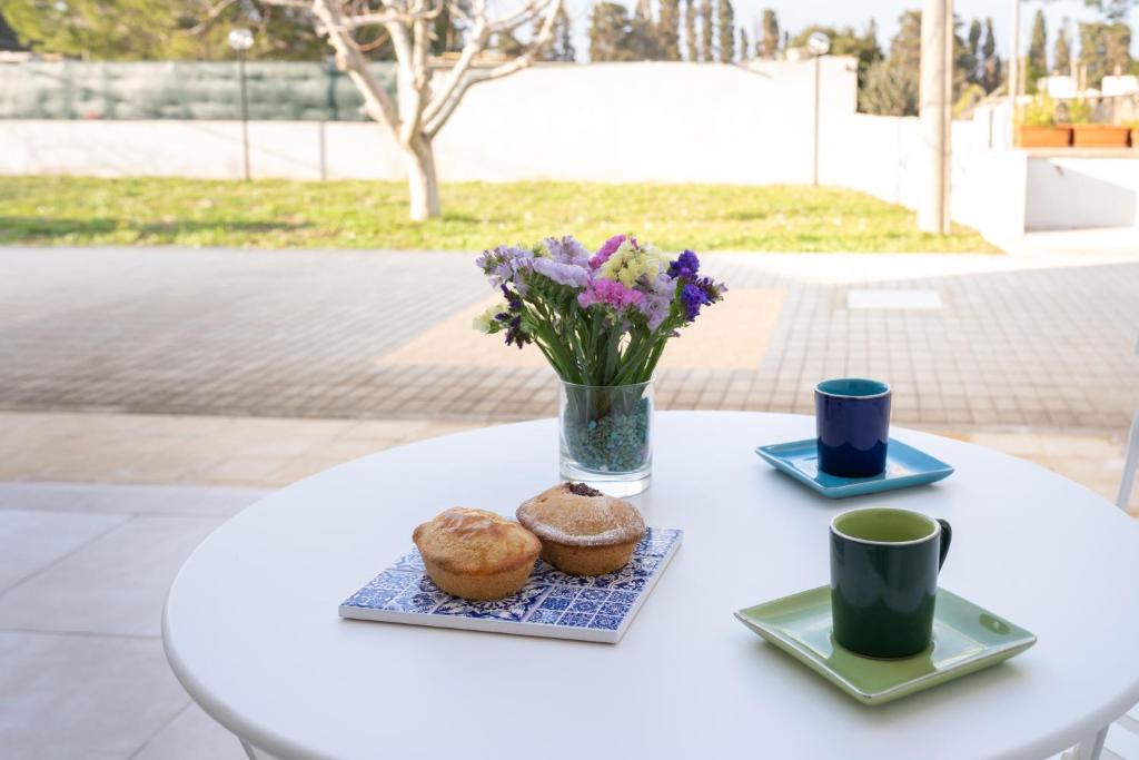 einen weißen Tisch mit zwei Muffins und einer Vase Blumen in der Unterkunft Smilax - Hydruntum Holiday Rooms in Otranto