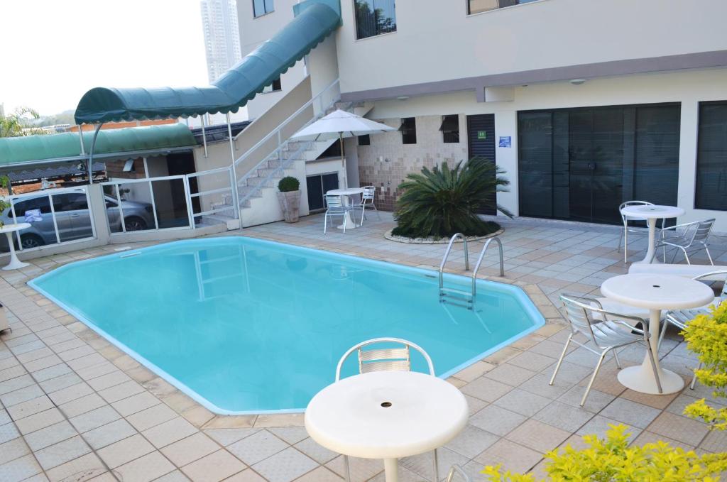 a pool with tables and chairs next to a building at Hotel Steinhausen in Blumenau