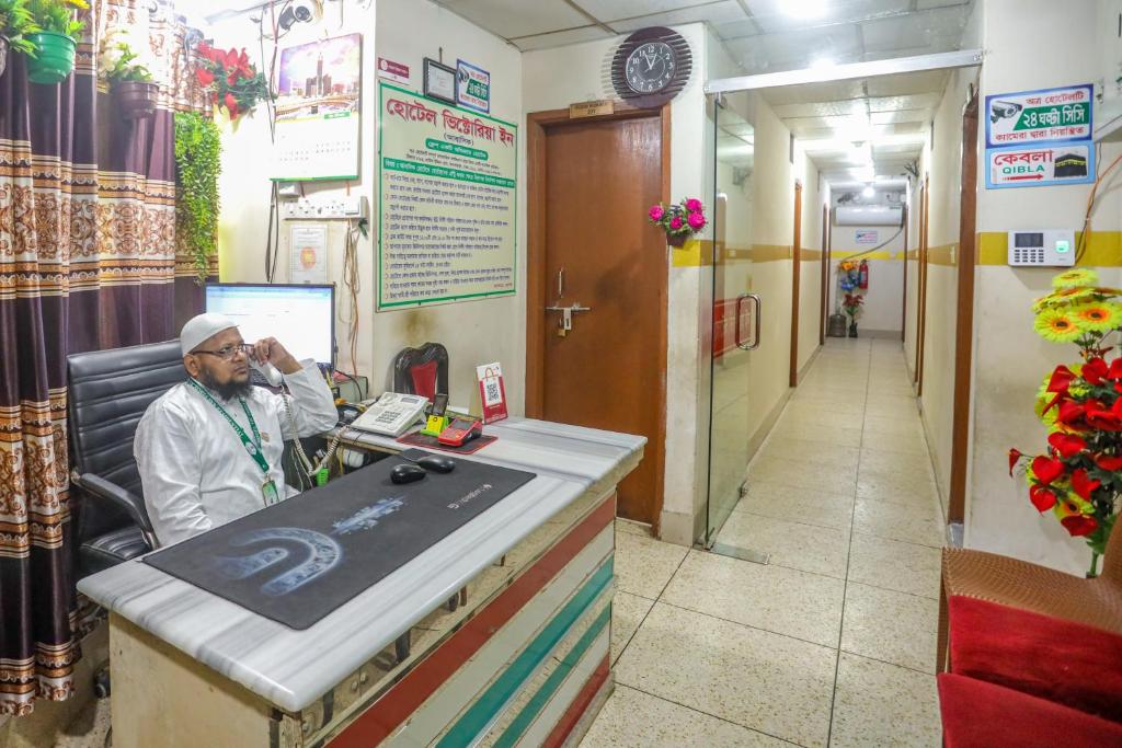 un hombre sentado en una caja registradora en una sala de espera en Hotel Victoria Inn (Nazimuddin Road), en Dhaka