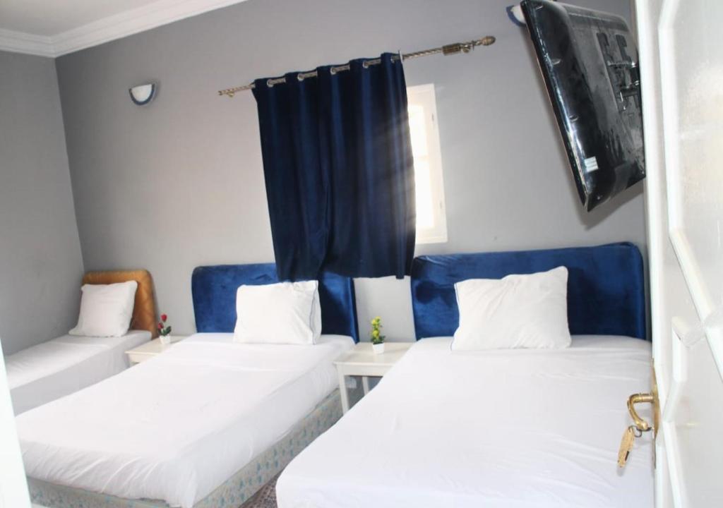 2 Betten in einem Zimmer mit blauen Vorhängen in der Unterkunft HOTEL ERRACHIDIA in Er Rachidia