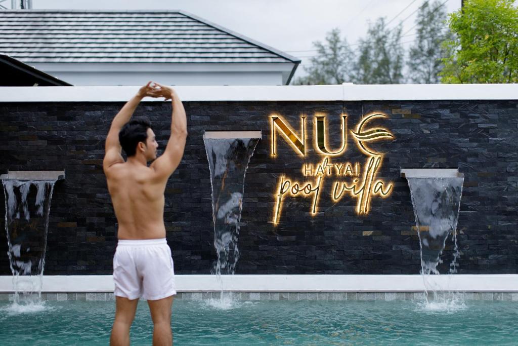 Nue Hatyai Pool Villa 147 في سونغكلا: رجل يقف في الماء أمام النافورة