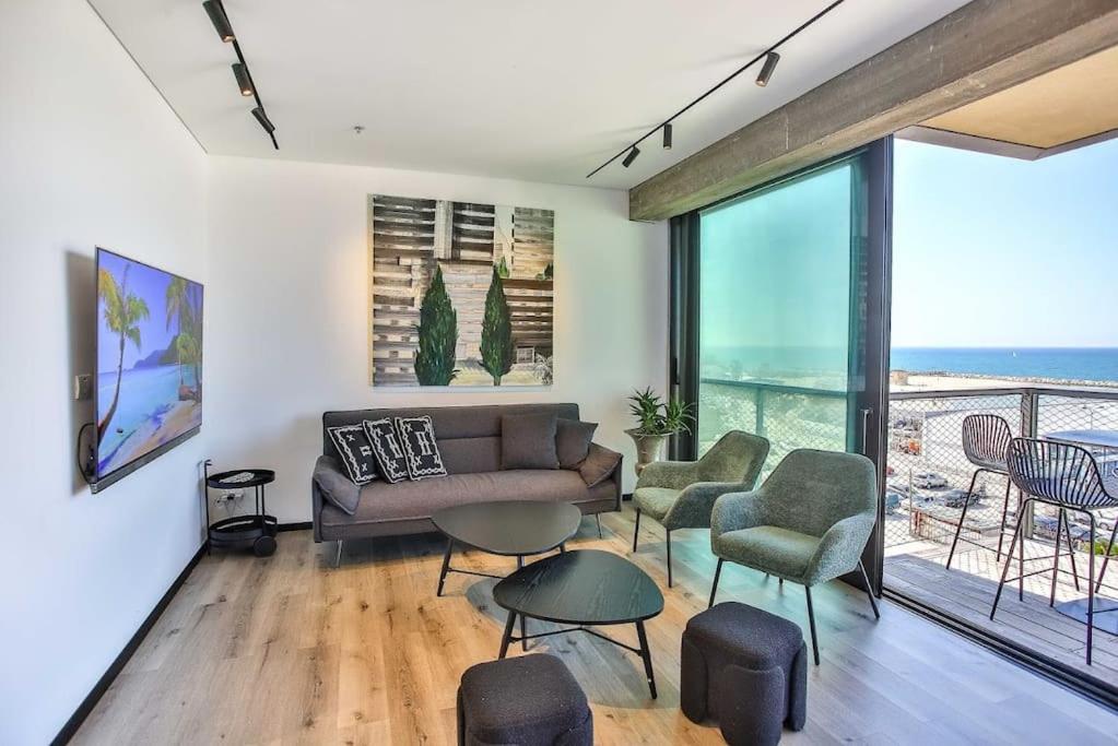 Stunning 1BR Beach Apartment في تل أبيب: غرفة معيشة مع أريكة وكراسي وشرفة