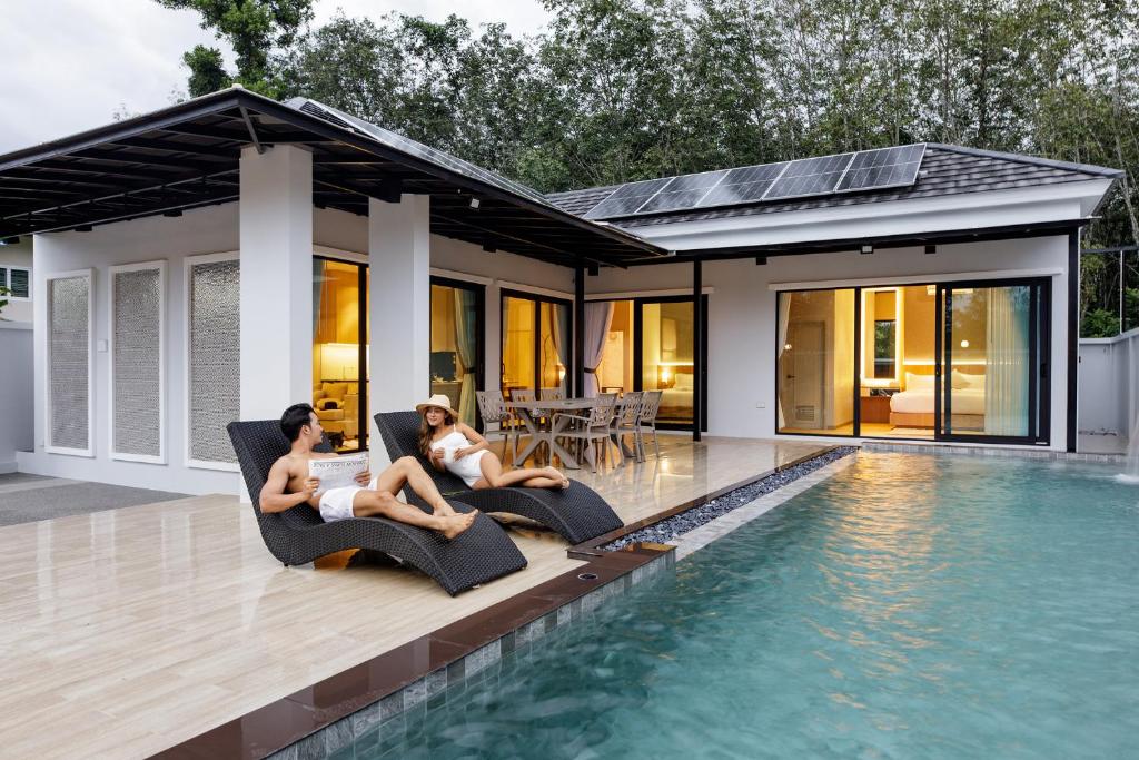 two women sitting on chairs next to a swimming pool at Nue Hatyai Pool Villa 145 
