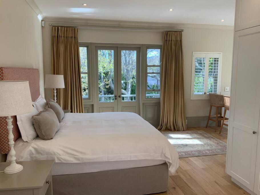 a bedroom with a large white bed and windows at The Alphen Cottage in Cape Town