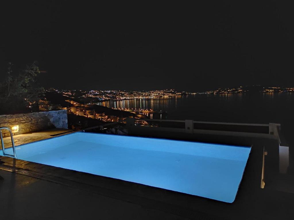 una piscina illuminata di notte su un tetto di Mykonian Luxury Villa Azure w Sea View and Pool ad Agios Stefanos
