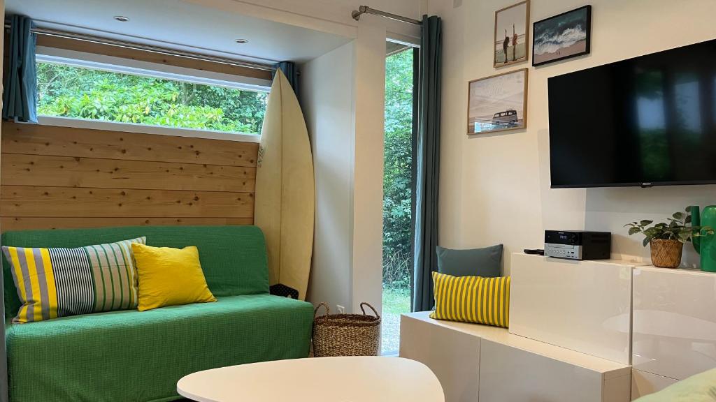een woonkamer met een groene bank en een televisie bij Le Bungalow in Bonningues-lès-Calais