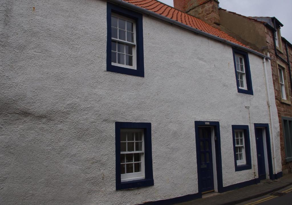 a white building with blue windows on a street at Smugglers Well in Cellardyke