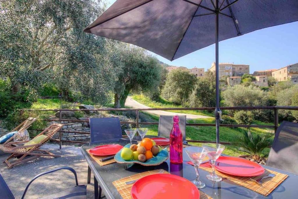- une table avec un bol de fruits et un parasol dans l'établissement A CasaLèna - Maison individuelle Balagne, à Urtaca