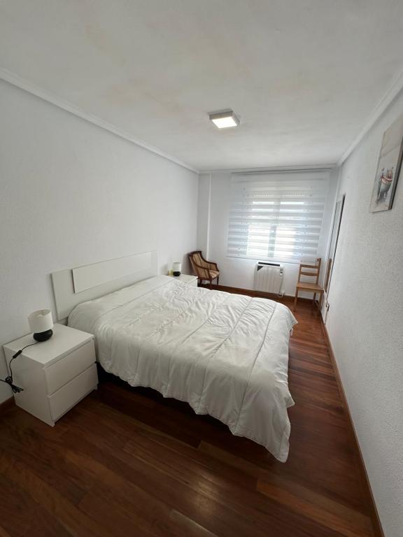 a white bedroom with a large bed and wooden floors at El Rincón del Faro - Parking incluido in San Vicente de la Barquera