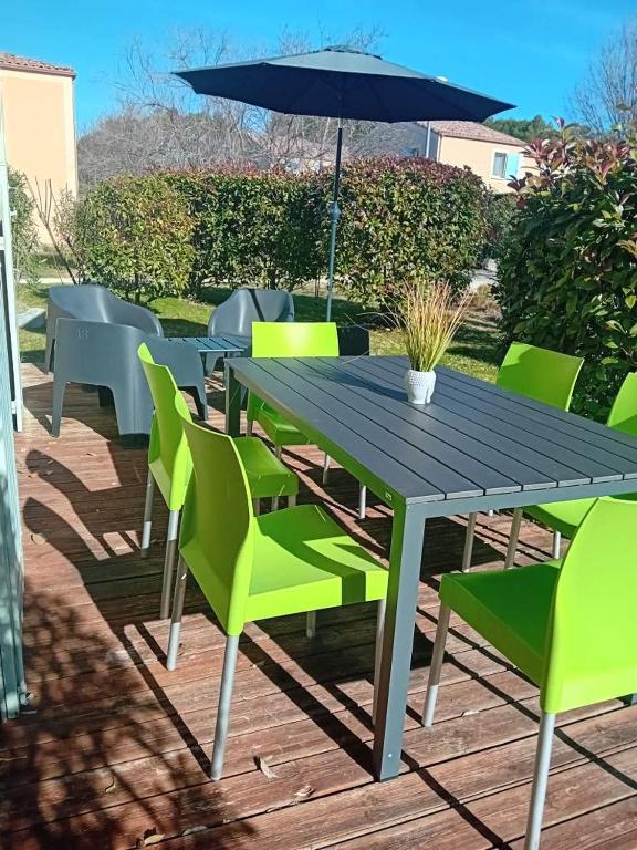 une table en bois avec des chaises vertes et un parasol dans l'établissement Résidence Les Demeures du Ventoux, à Aubignan