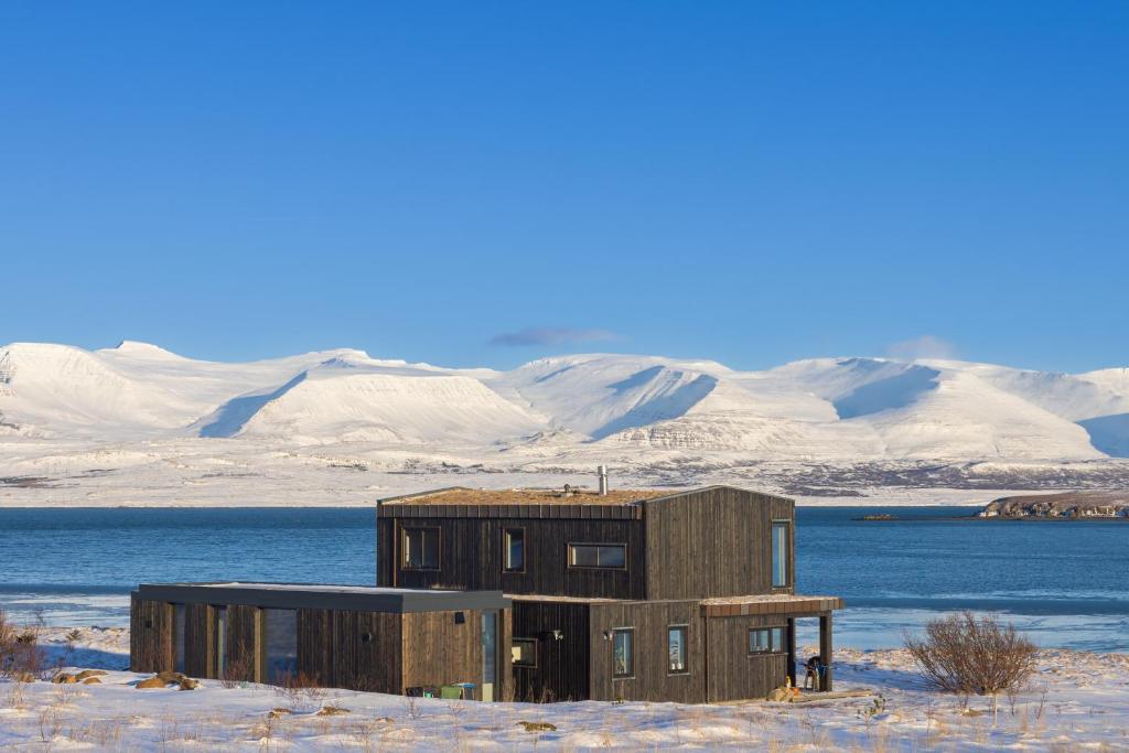 una casa en la nieve con montañas en el fondo en The Oceanfront Private northern lights villa., en Reynivellir