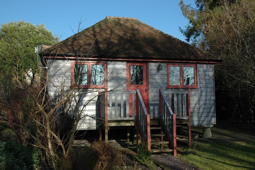 The Granary at Palm Tree House in S.E. Kent في Lyminge: منزل صغير بباب احمر ونوافذ