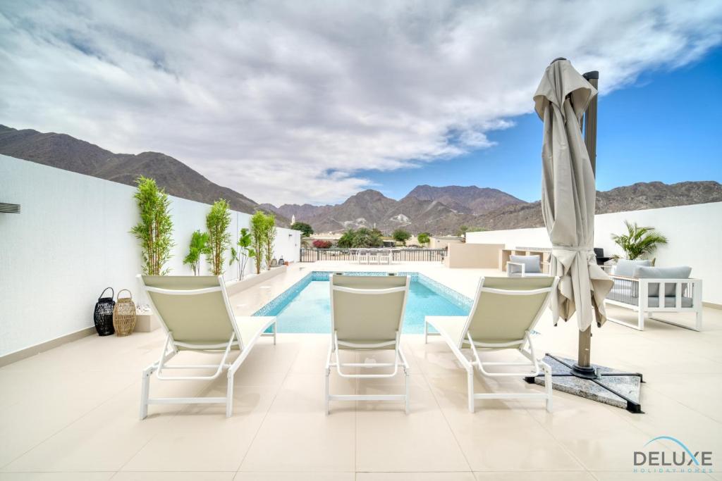 a patio with chairs and a pool and a umbrella at Beautiful 3BR Villa with Assistant Room Al Dana Island, Fujairah by Deluxe Holiday Homes in Fujairah