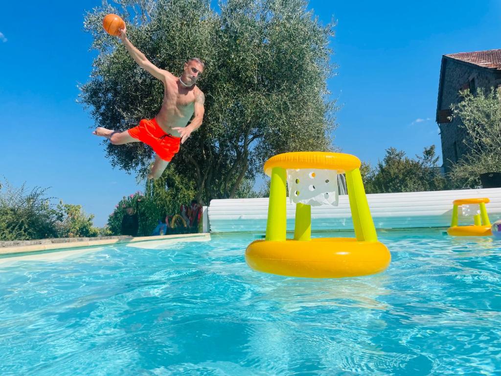 a man jumping into a swimming pool with a basketball at Le Planzollais in Planzolles