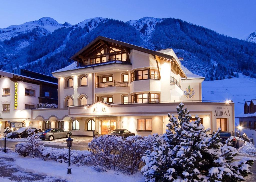 um grande edifício na neve com montanhas ao fundo em Hotel Albona em Ischgl