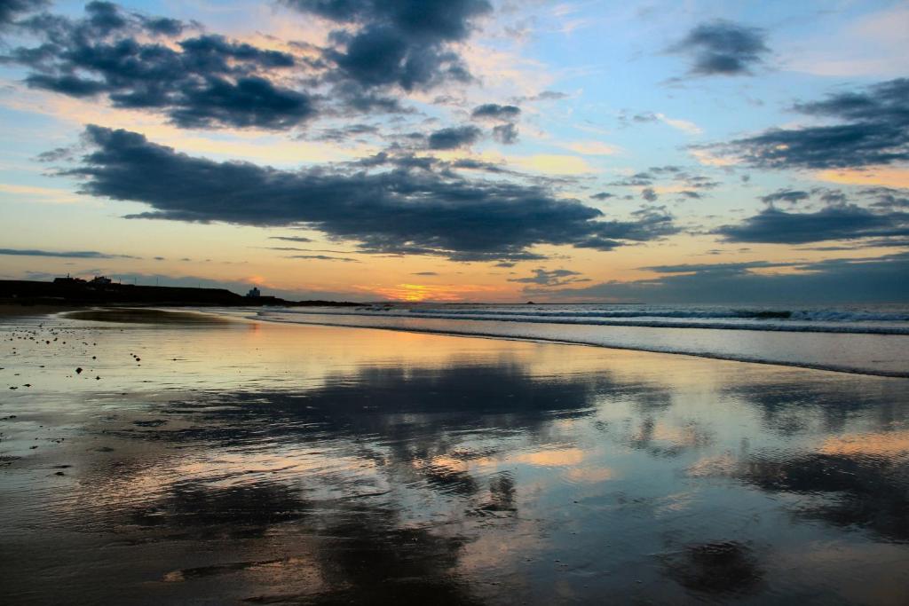 a sunset on a beach with the reflection of the clouds at Pintail Apartment Bamburgh in Bamburgh