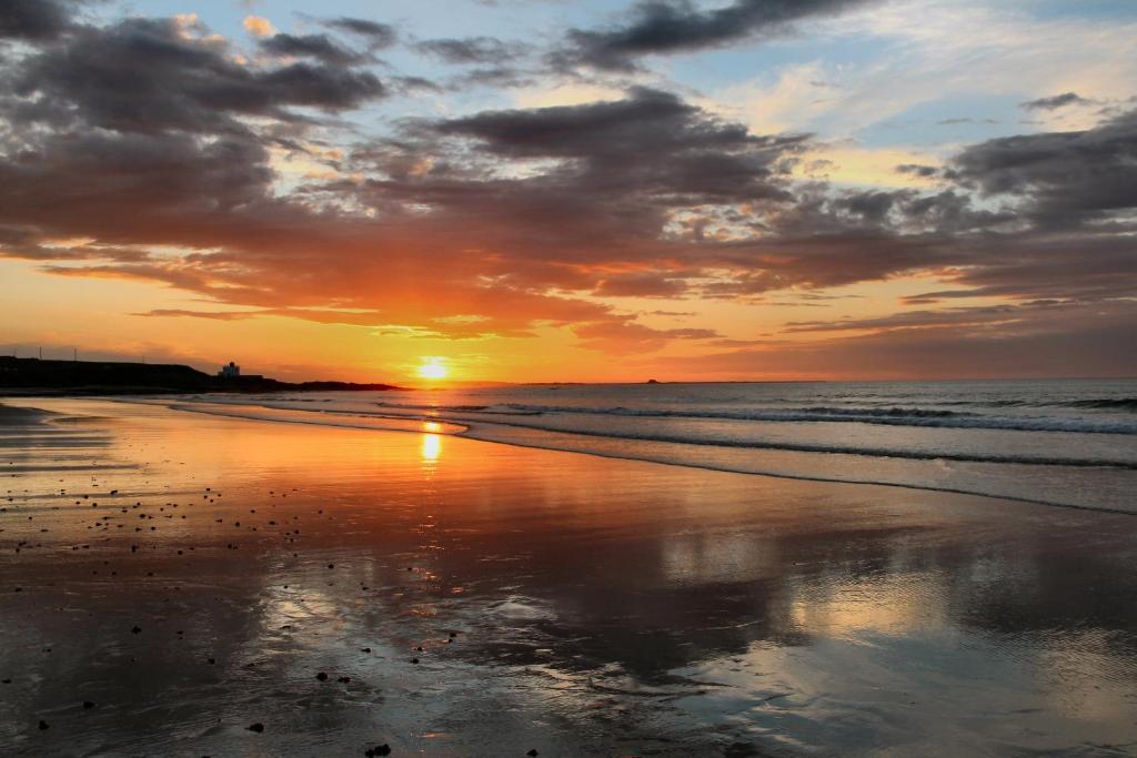 a sunset on a beach with the ocean at Pintail Apartment Bamburgh in Bamburgh