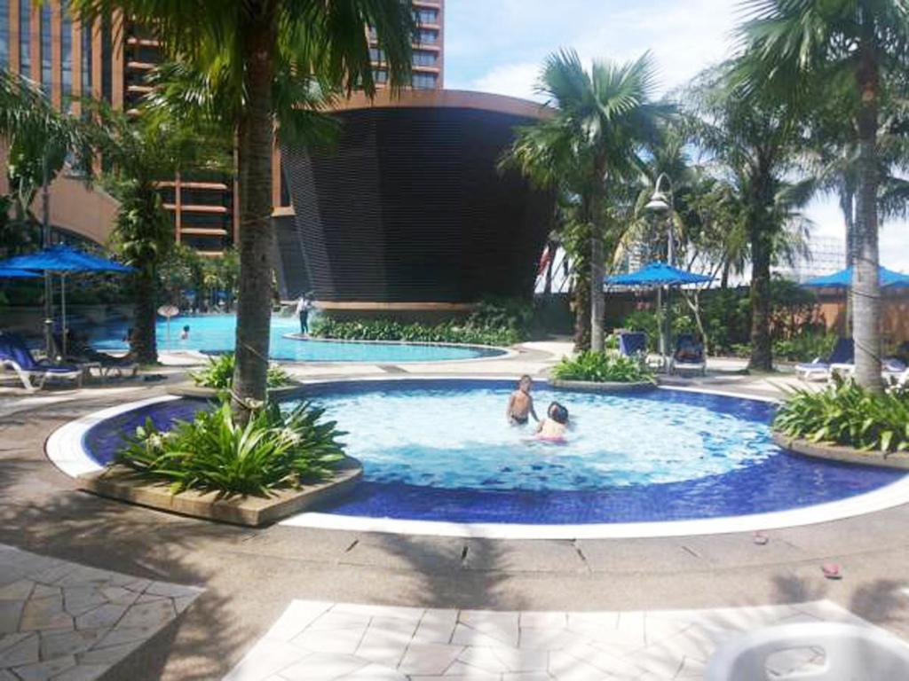 two people in a swimming pool with palm trees at Bintang Lux B&B Suites Times Square KL in Kuala Lumpur