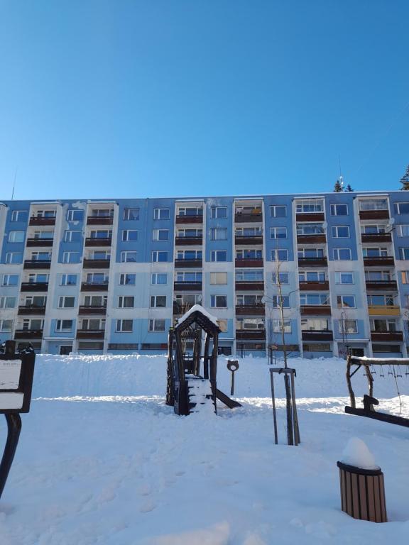 un gran edificio de apartamentos con un parque infantil en la nieve en Apartmán Špičák, en Jiřetín pod Bukovou