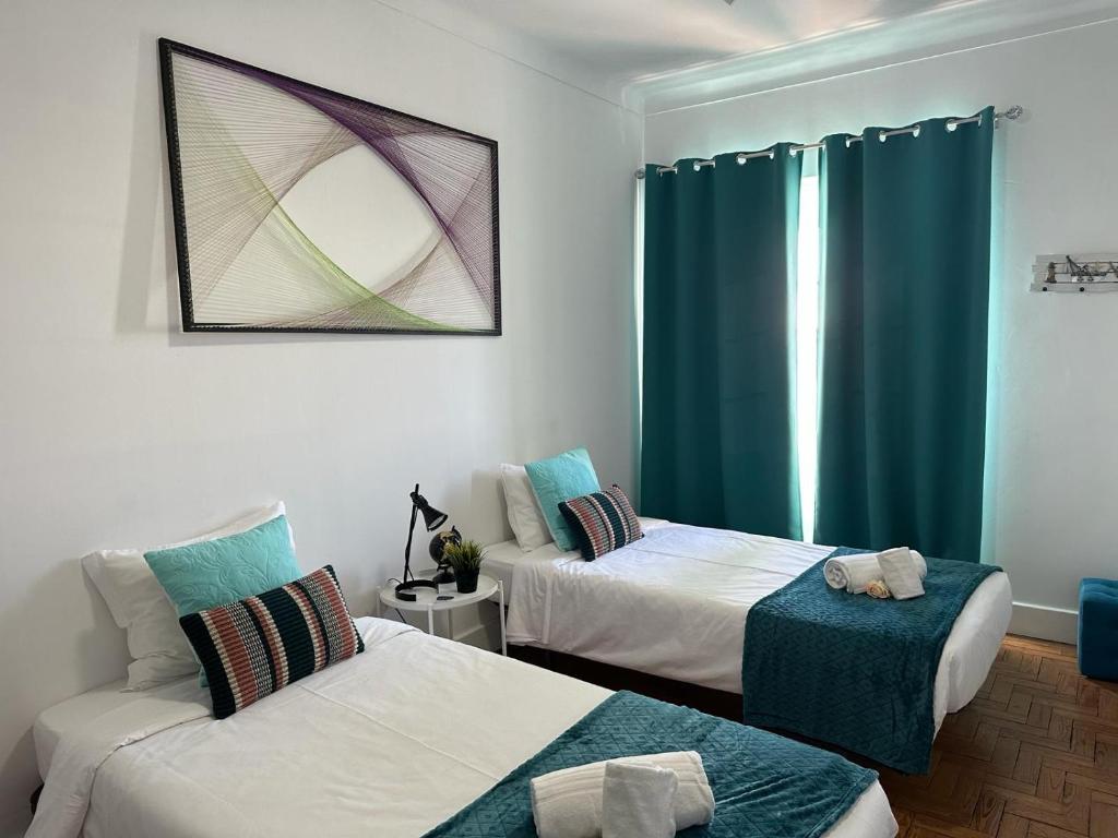 a room with two beds and a window with blue curtains at Alojamentos Vista Mar-Luisa Todi in Setúbal