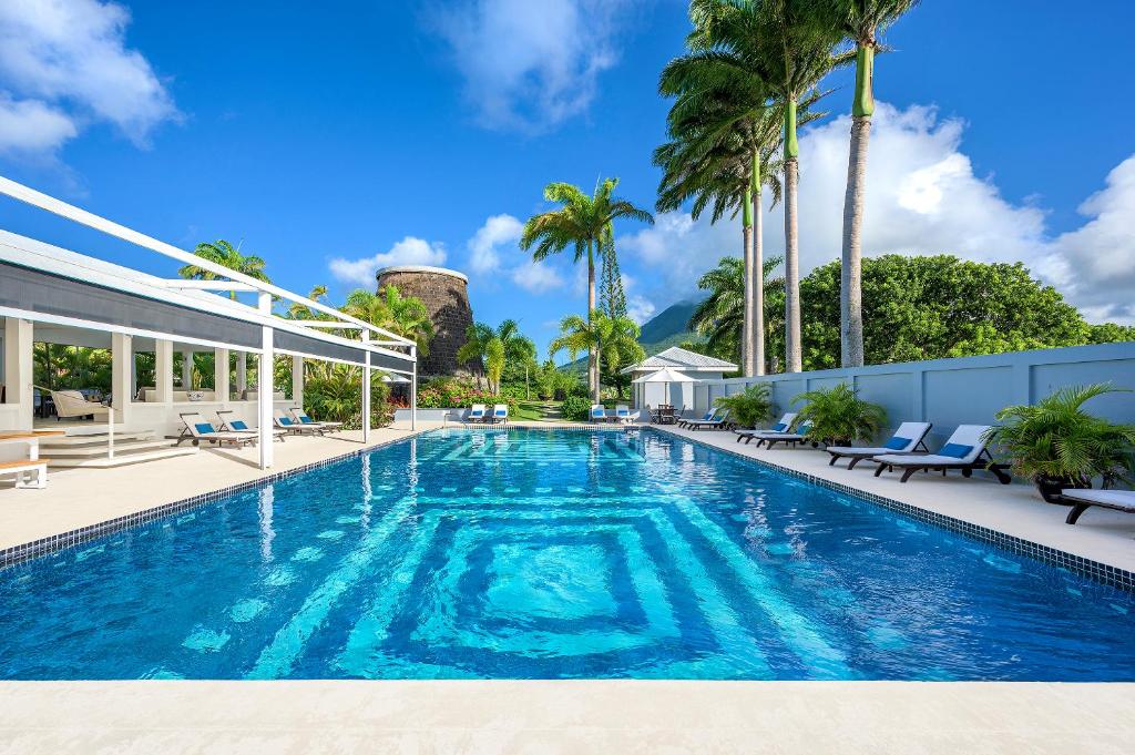 a swimming pool with palm trees and a building at Montpelier Plantation & Beach in Nevis