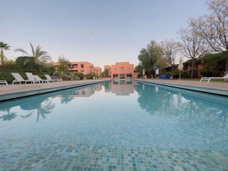 a large swimming pool with chairs and a building at Appartement cosy et calme avec jardin et piscine in Marrakech